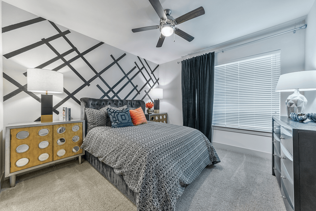 A bedroom with a bed, a ceiling fan, and a wall with a pattern of black lines.