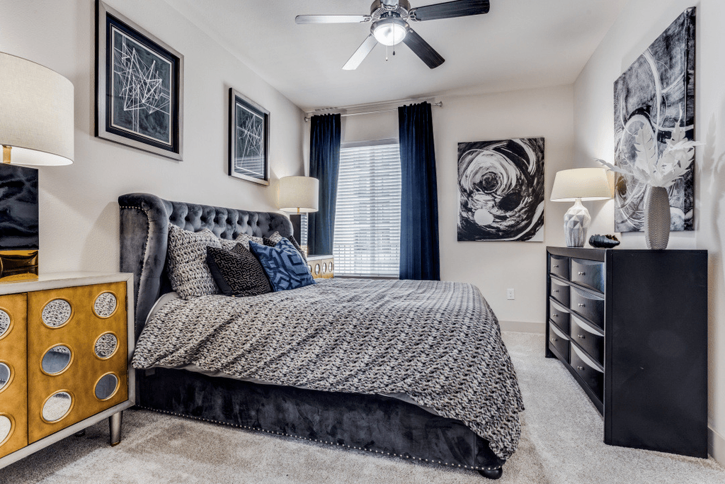 A bedroom with a large bed, a ceiling fan, and a dresser.