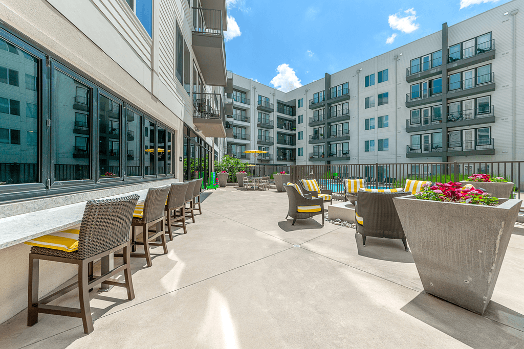 A patio with chairs and planters is surrounded by buildings.