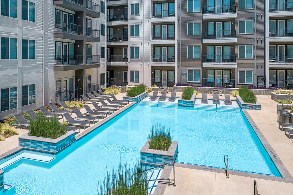 A large swimming pool surrounded by lounge chairs and buildings.