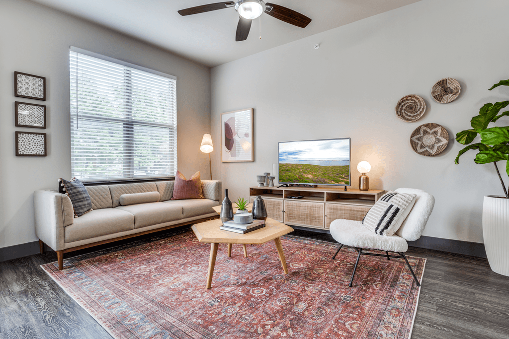 A living room with a beige sofa, a wooden coffee table, a white chair, and a ceiling fan.