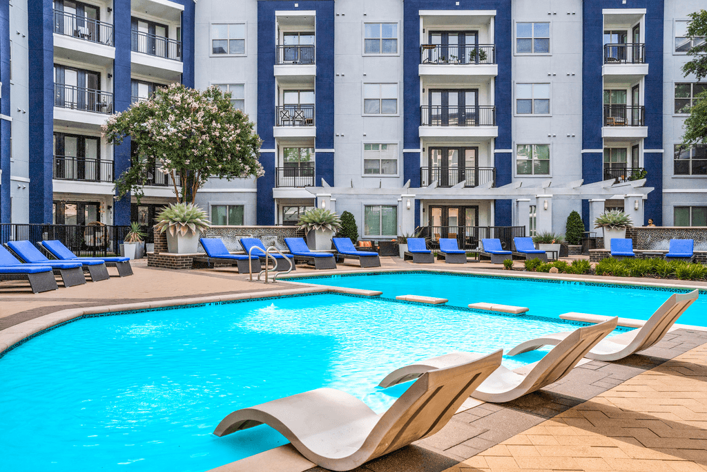 A large swimming pool with lounge chairs in front of a multi-story apartment building.