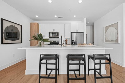 A modern kitchen with white cabinets and a white island with three black barstools.