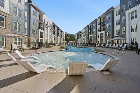 A pool surrounded by white lounge chairs in front of apartment buildings.