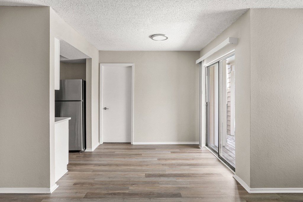 an empty hallway with a door to a kitchen and a refrigerator