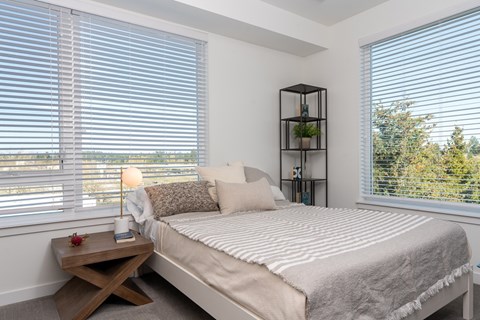 A bedroom with a bed, a table, and a window with blinds.