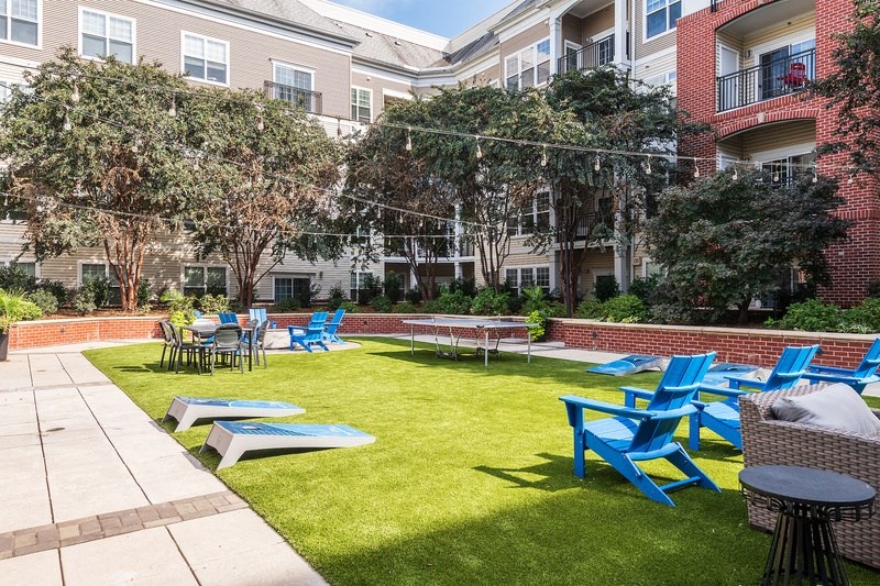 an outdoor lounge area with blue chairs and tables in front of an apartment building