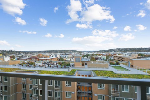 A view from a high-rise building looking out over a cityscape with buildings of various sizes and a clear blue sky with scattered clouds.