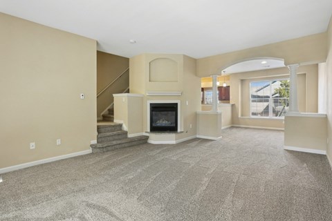 A spacious living room with a fireplace and a staircase.