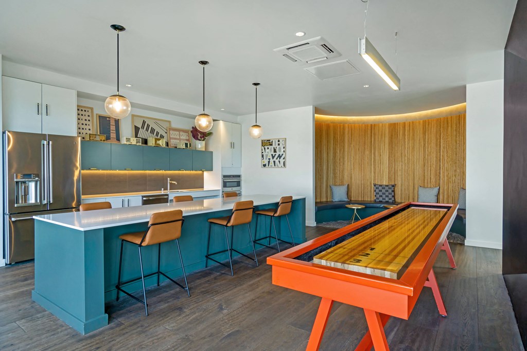 a game room with a shuffleboard table and a kitchen