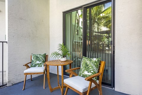 A patio with a table and two chairs with green cushions.