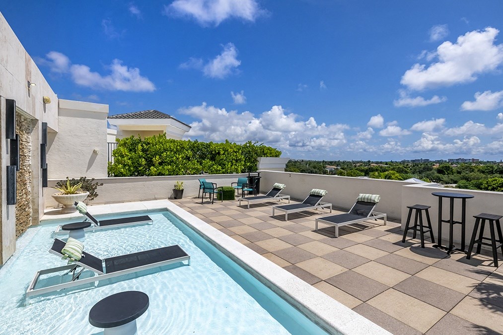 a swimming pool with lounge chairs on a rooftop terrace with a blue sky