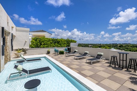 A pool with a table and chairs is surrounded by a tiled floor.