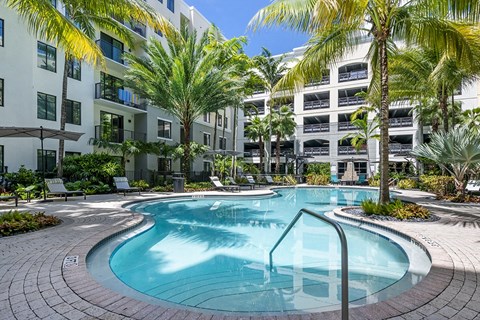 A swimming pool surrounded by palm trees and apartment buildings.