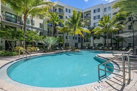 A swimming pool surrounded by palm trees and apartment buildings.