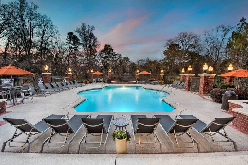 A pool surrounded by chairs and umbrellas with trees in the background.