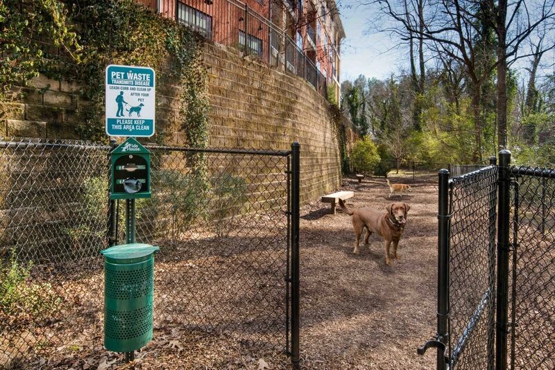 A sign for pet waste is displayed on a post next to a green trash can.
