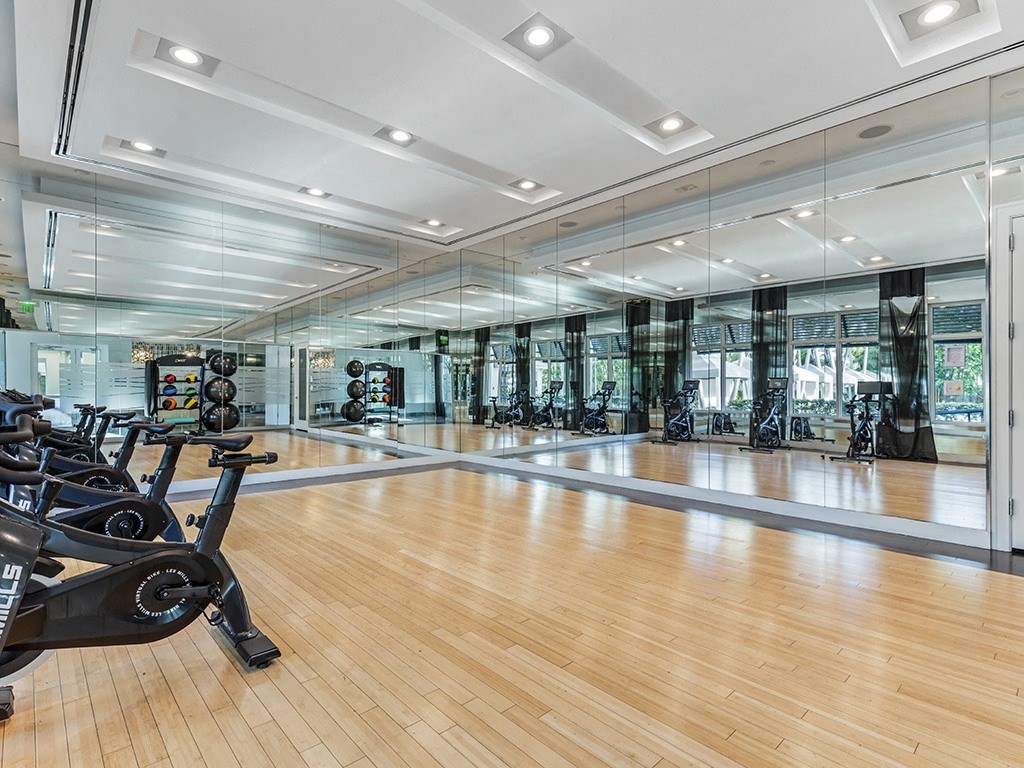 the gym has a glass walled cardio area and a wood floor