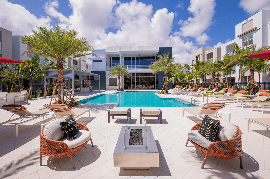 A pool surrounded by chairs and palm trees.