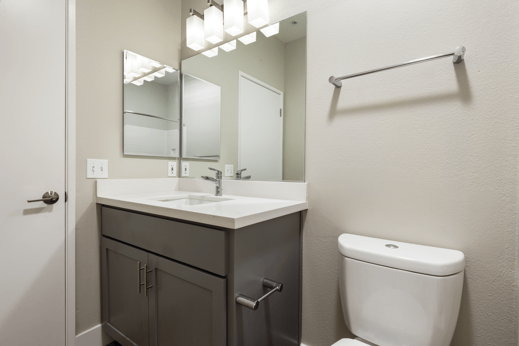 A bathroom with a toilet, sink, mirror, and towel rack.