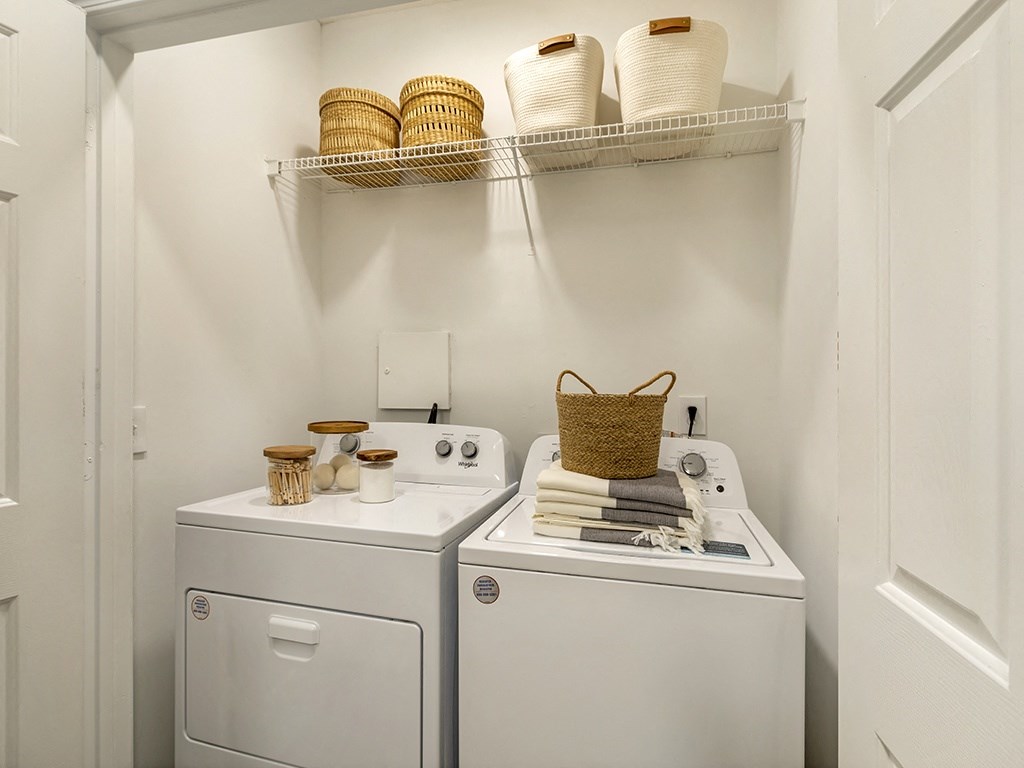 a small laundry room with white appliances and a shelf above the washer and dryer