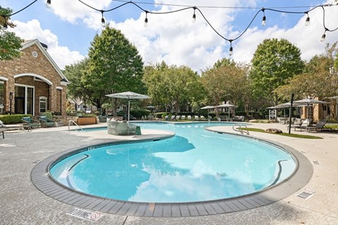 A large outdoor swimming pool surrounded by trees and a building.