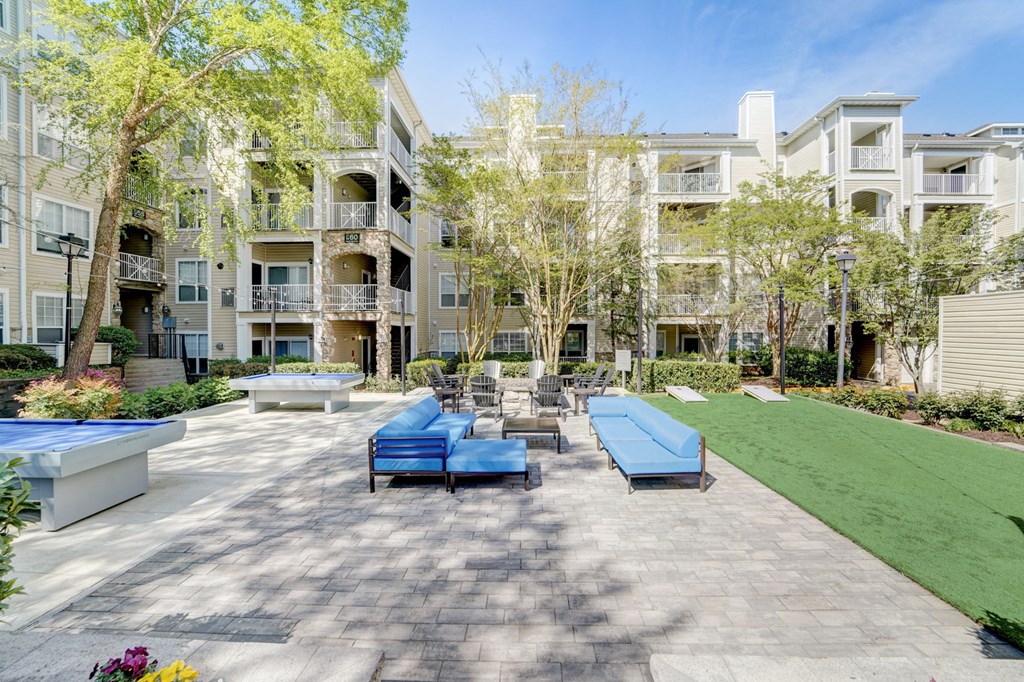 an outdoor patio with blue couches and chairs and a lawn with trees