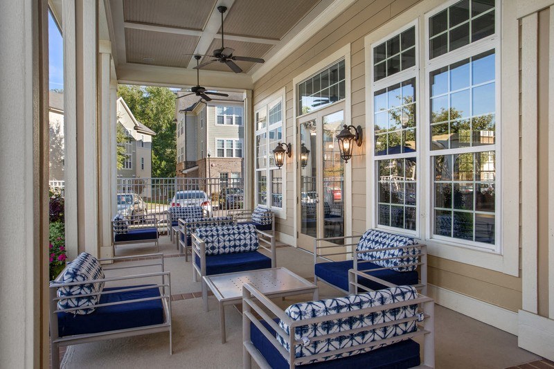 a porch with blue chairs and a coffee table in front of a row of windows