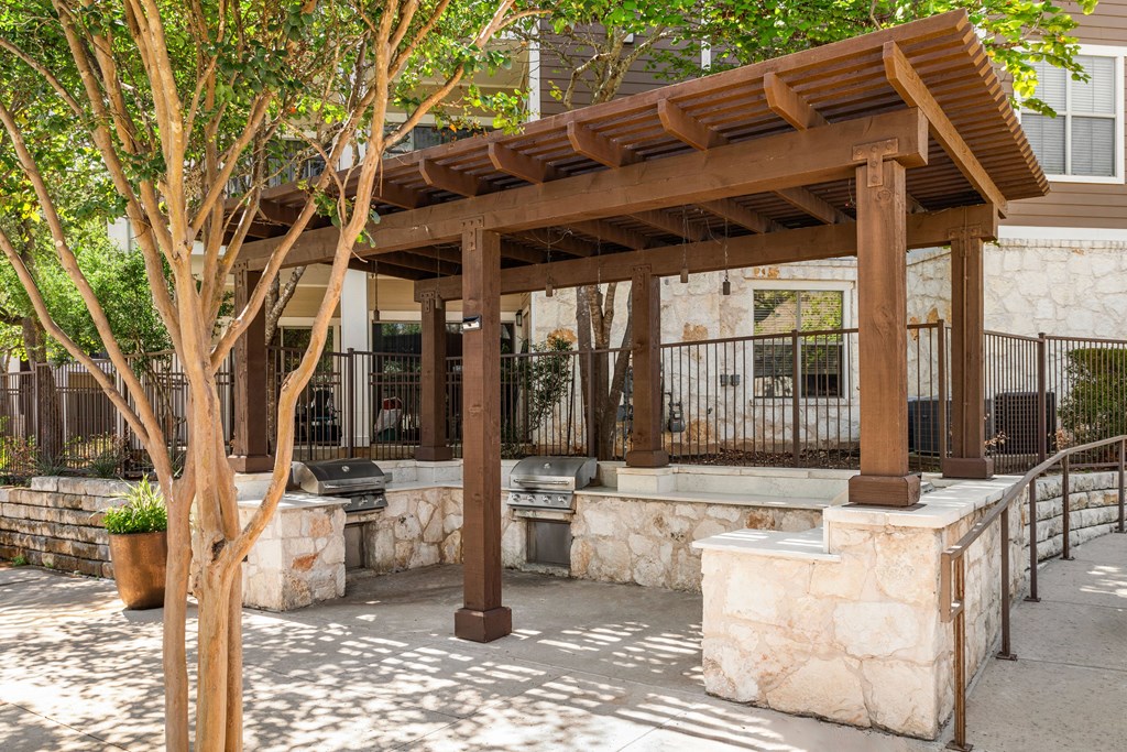 a stone patio with a wooden pavilion and trees