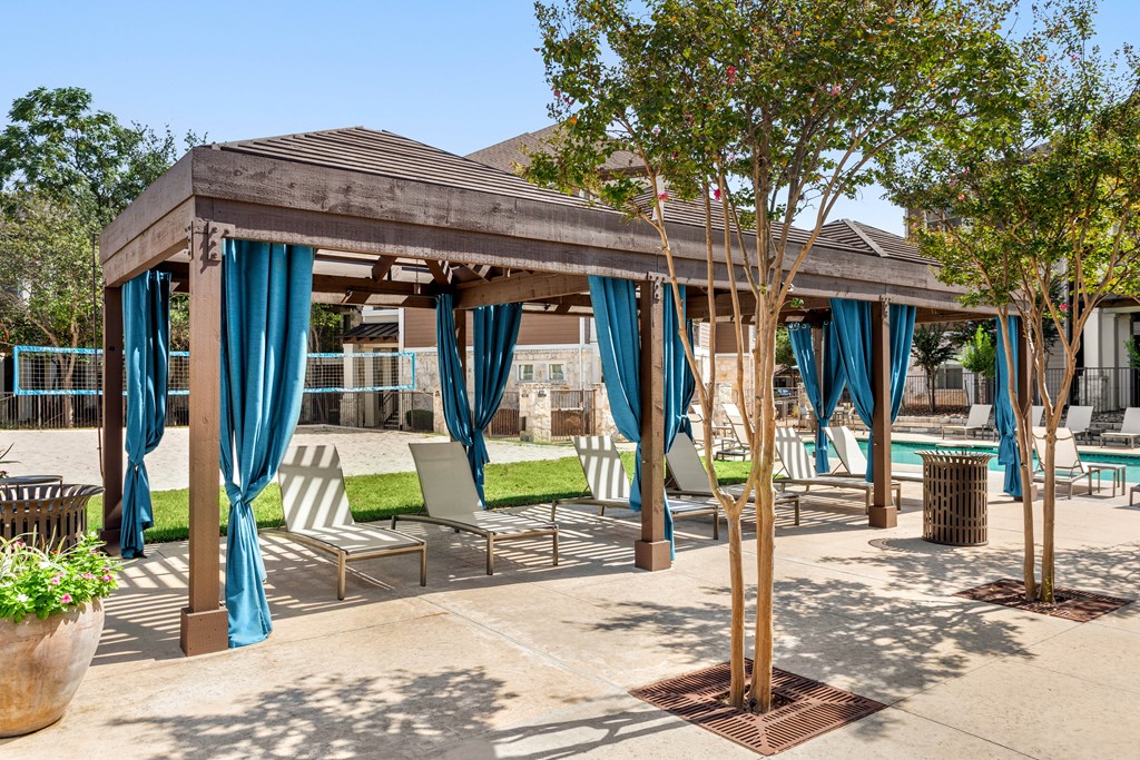 a gazebo with blue curtains and chairs and trees