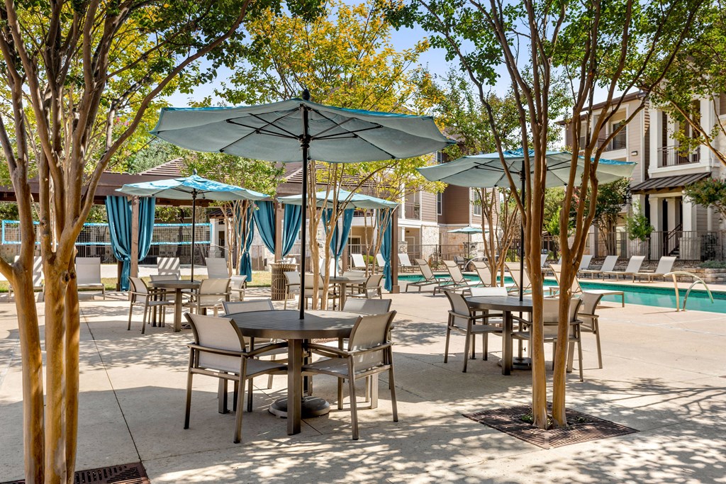 a patio with tables and umbrellas near a swimming pool