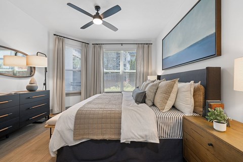A bedroom with a large bed, a ceiling fan, and a painting on the wall.