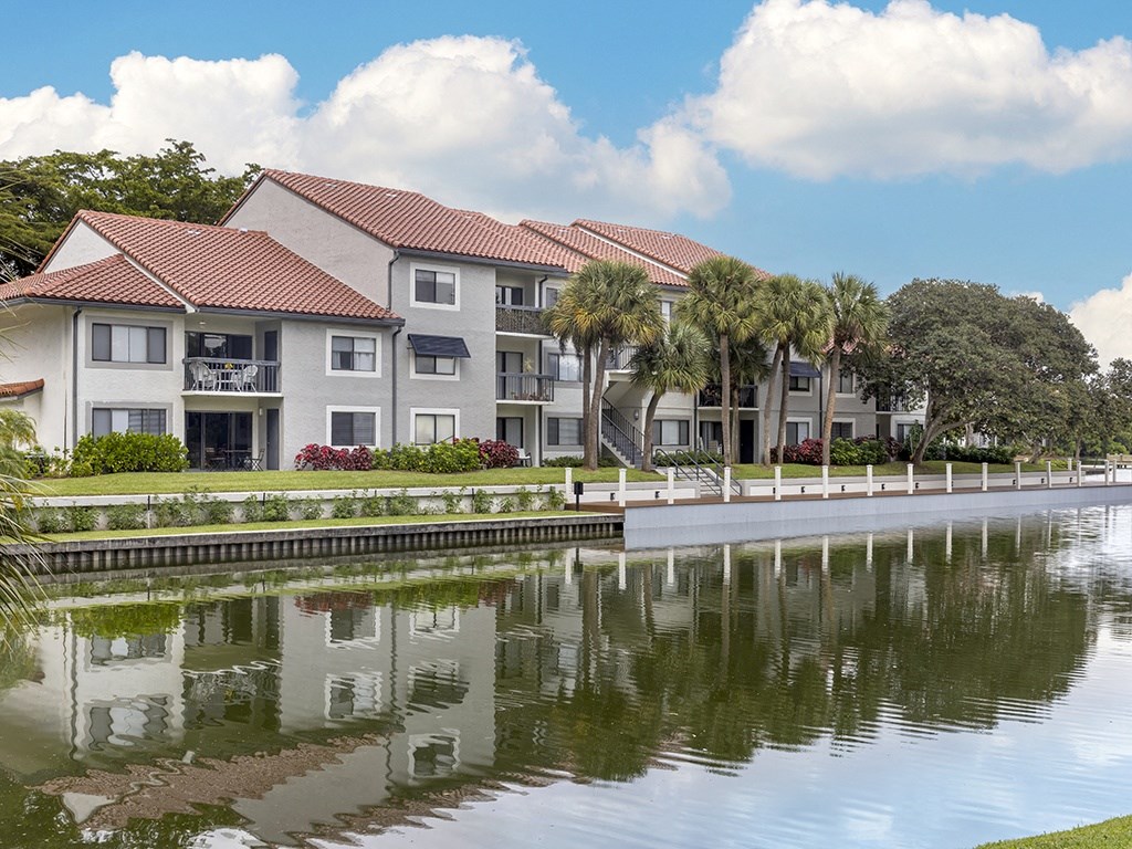 A building with a red roof is reflected in the water in front of it.