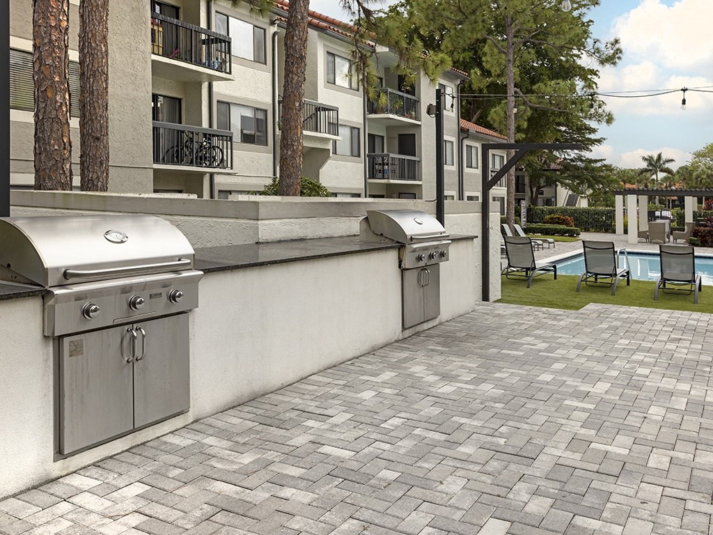 A patio with a grill and chairs is in front of a building.
