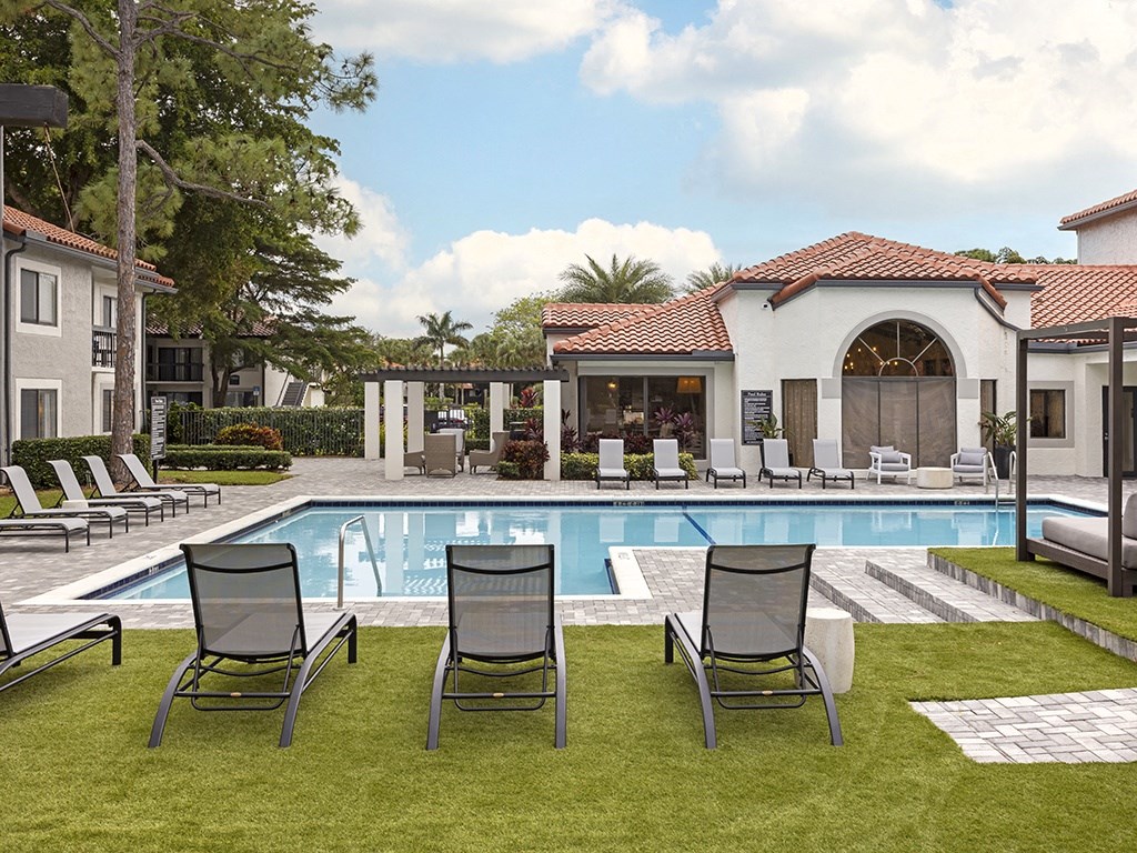 A pool surrounded by lawn chairs and a building in the background.