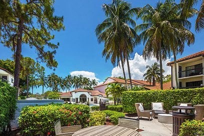 A house with a red roof and a wooden deck surrounded by greenery and palm trees.