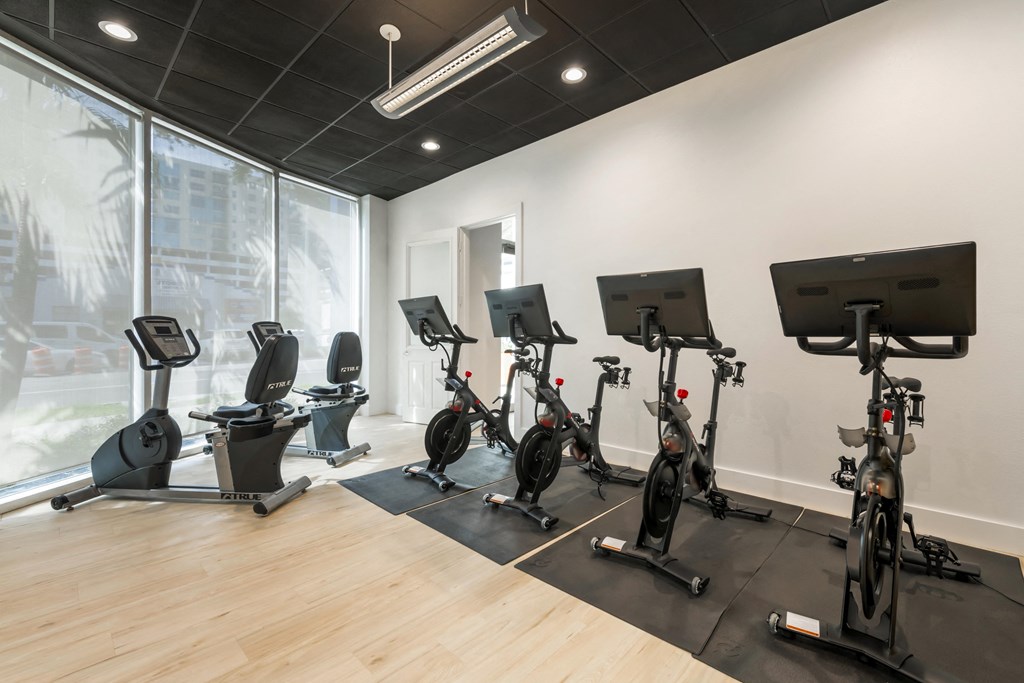 a gym with various exercise bikes on the floor and a large window