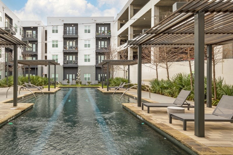 a swimming pool with lounge chairs and umbrellas in front of an apartment building