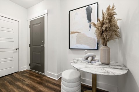 A grey door is in a white hallway with a framed picture on the wall.