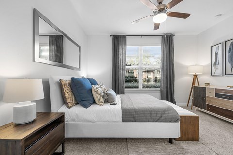 A bedroom with a large bed, a ceiling fan, and a window with curtains.