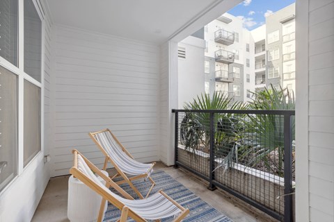 two chairs and a rug on a balcony with a view of an apartment building