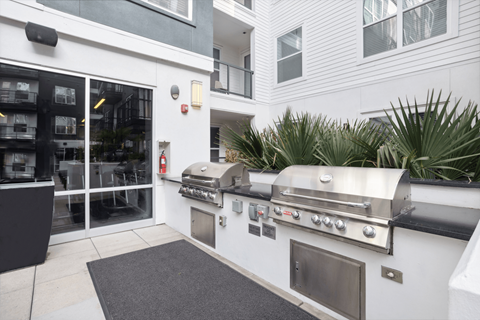 the outdoor grill area of a white building with stainless steel appliances