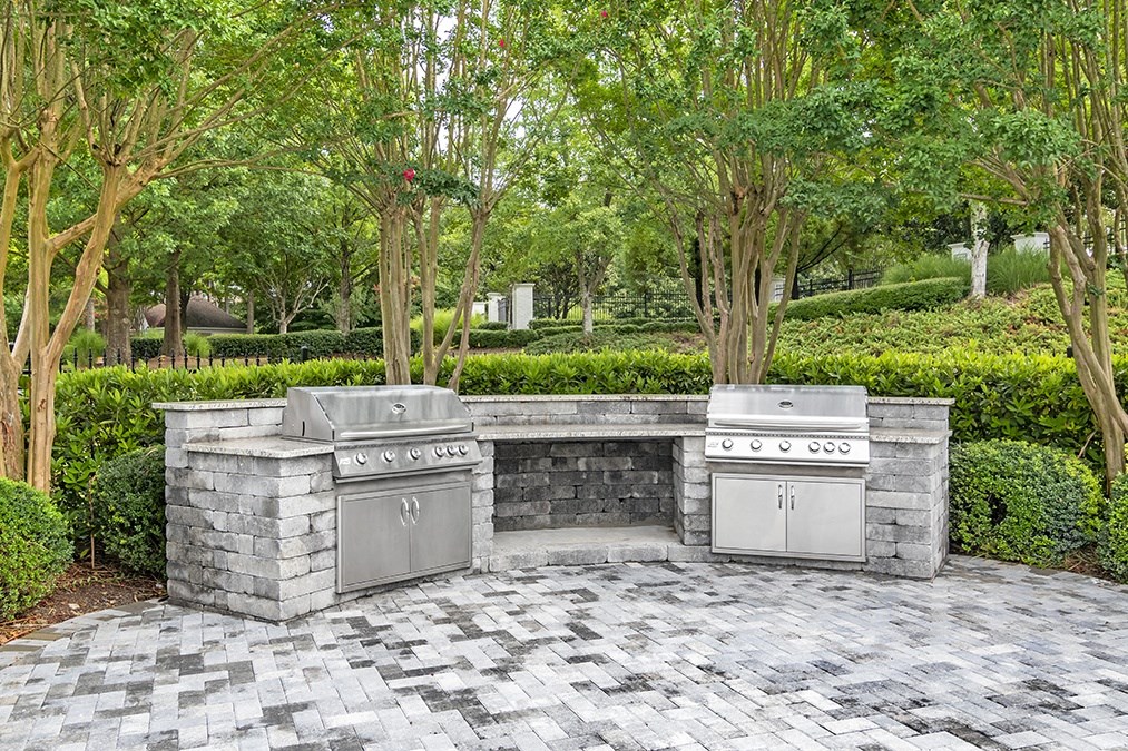 an outdoor kitchen with two stainless steel appliances on a stone patio