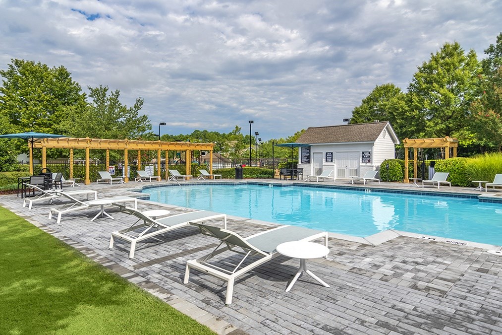 a swimming pool with white deck chairs and a house in the background