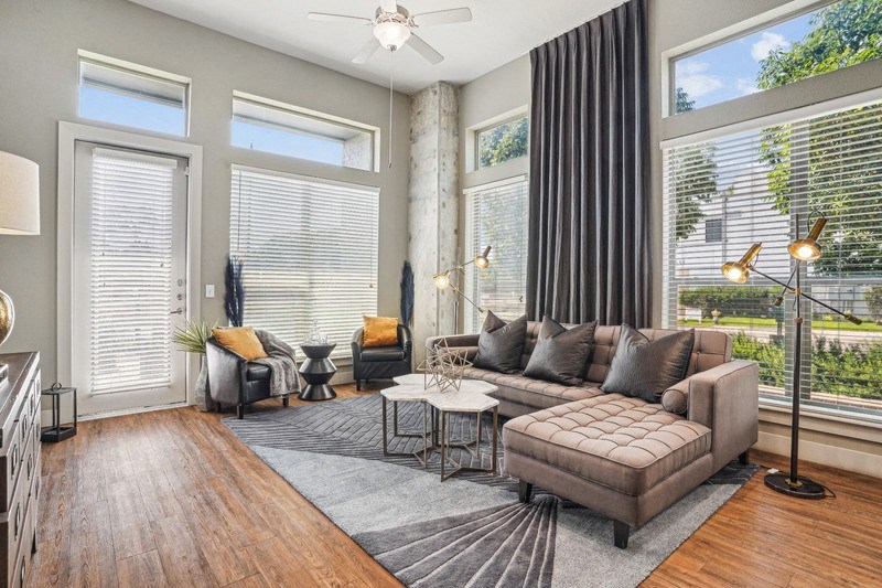 a room with a couch in the middle and big windows behind it