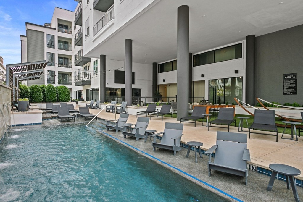 a swimming pool with lounge chairs and umbrellas in front of an apartment building
