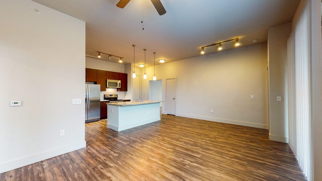 an empty living room with a kitchen and a ceiling fan