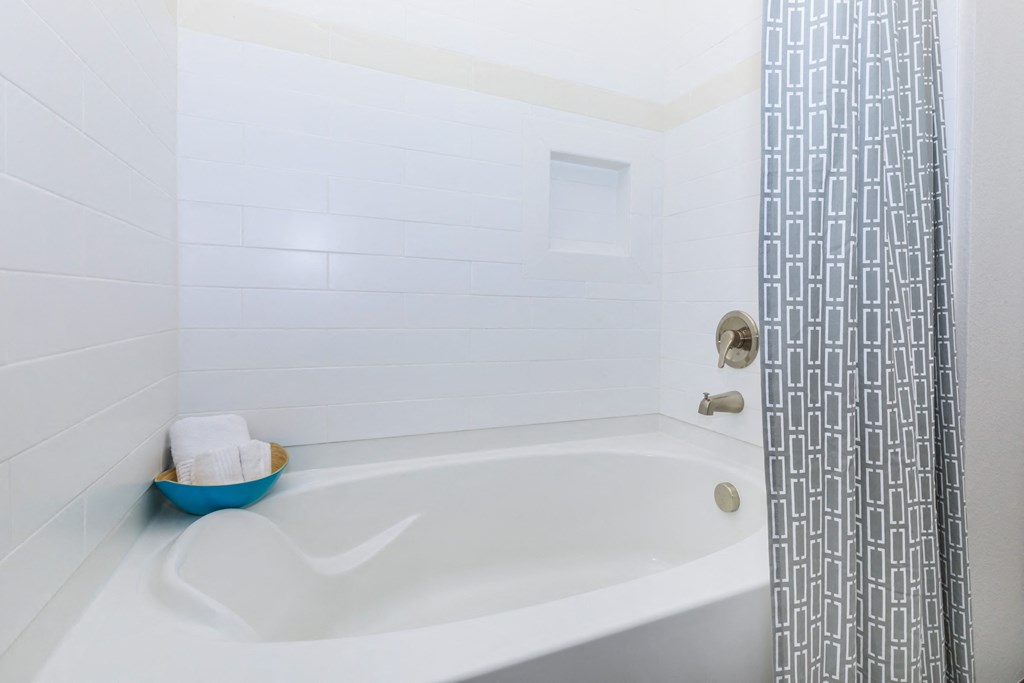 A white bathtub with a blue bowl on the side and a shower curtain.