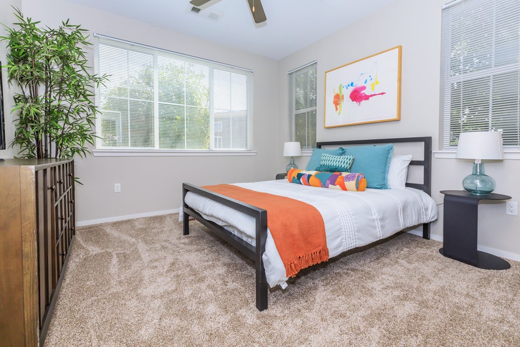 A bedroom with a bed, a potted plant, and a painting on the wall.