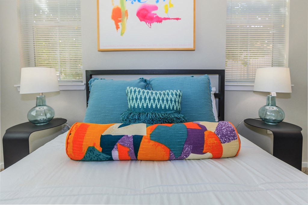 A bed with a white comforter and a blue pillow with a white design on it.